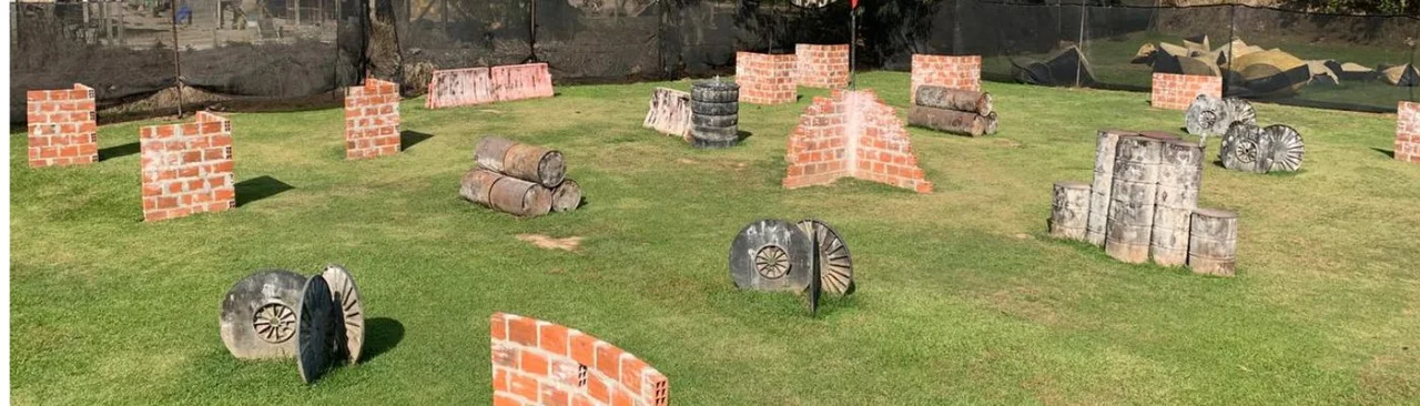 Campo al aire libre de Estrategia Paintball, con obstáculos de madera, llantas y barreras sobre el césped